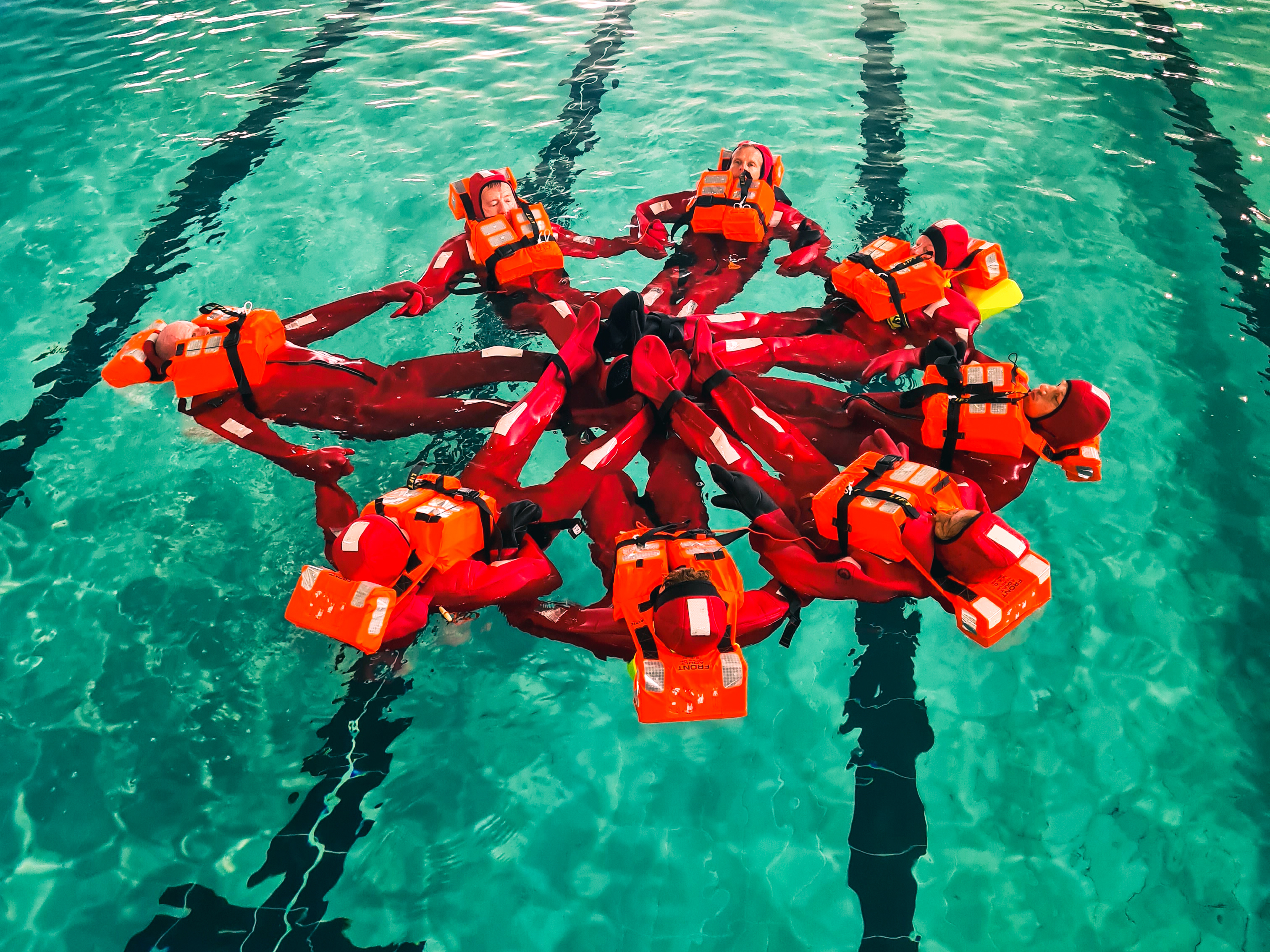 People wearing red immersion suits floating on top of the water in a circle