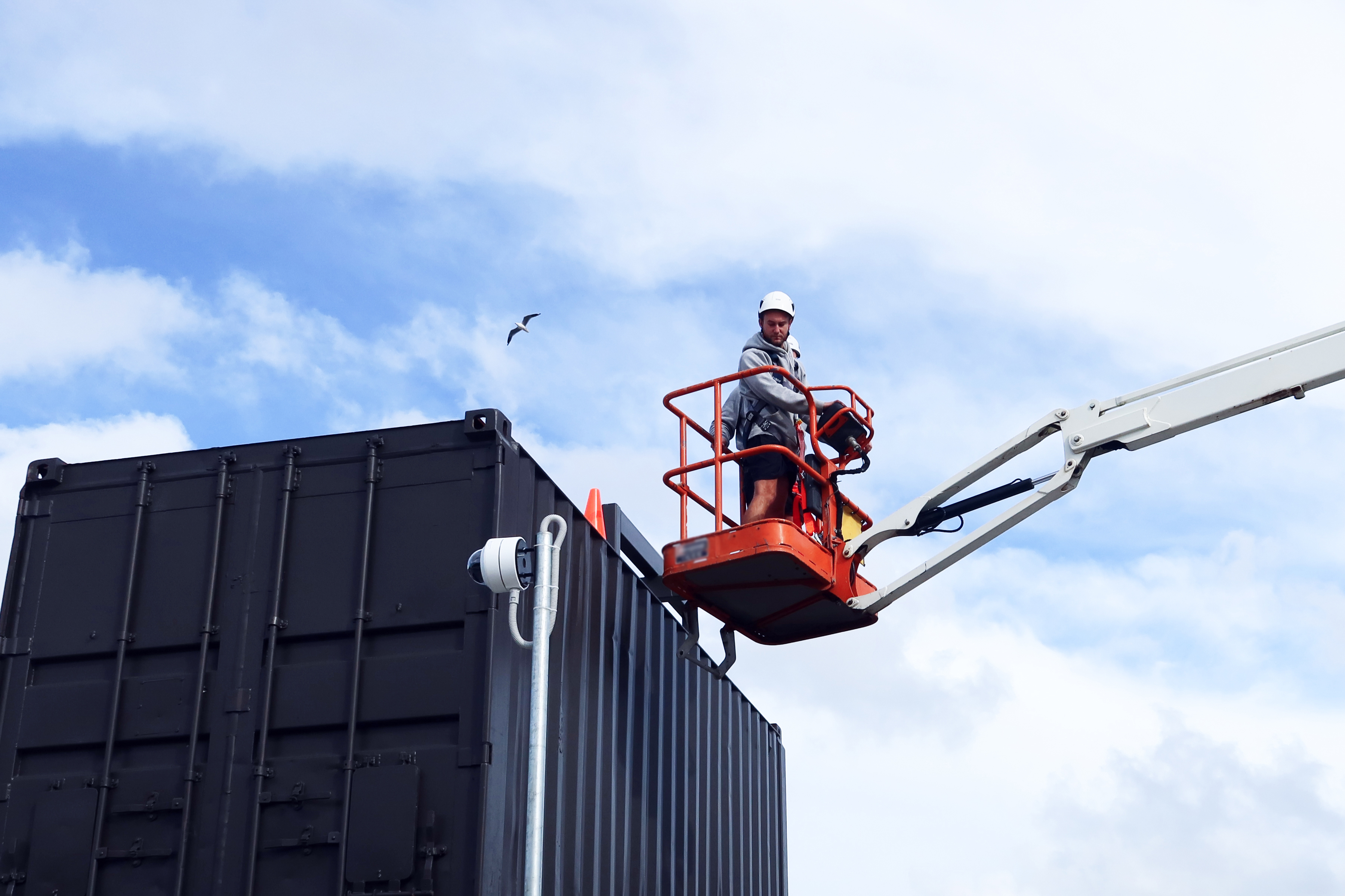 Two workers using an elevated work platform in the air above a shipping container